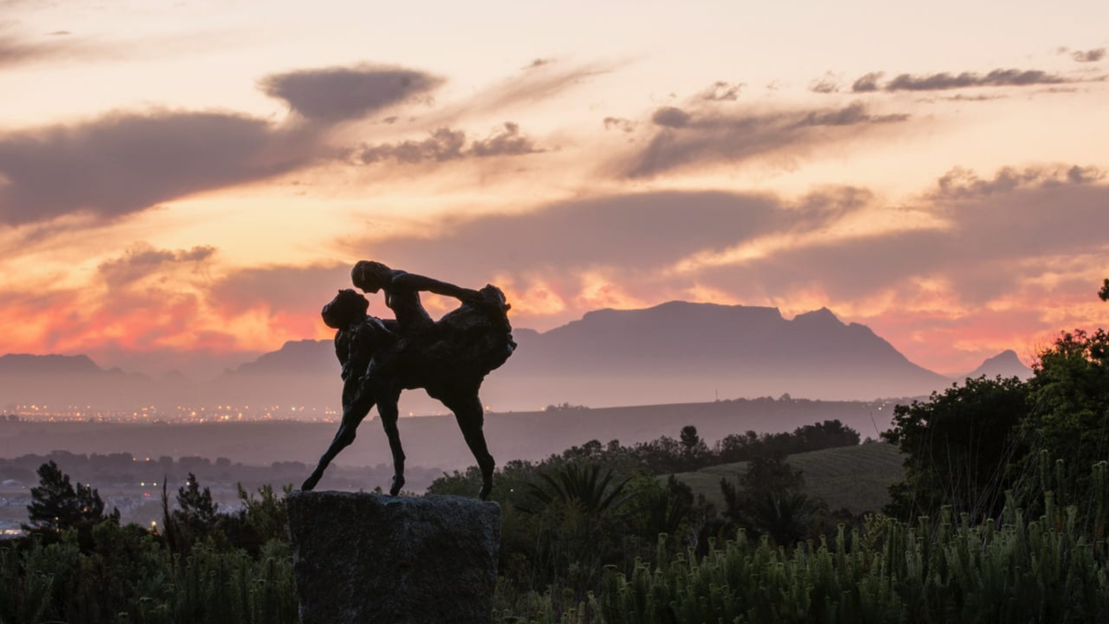 A sculpture over vineyards and mountains at sunset
